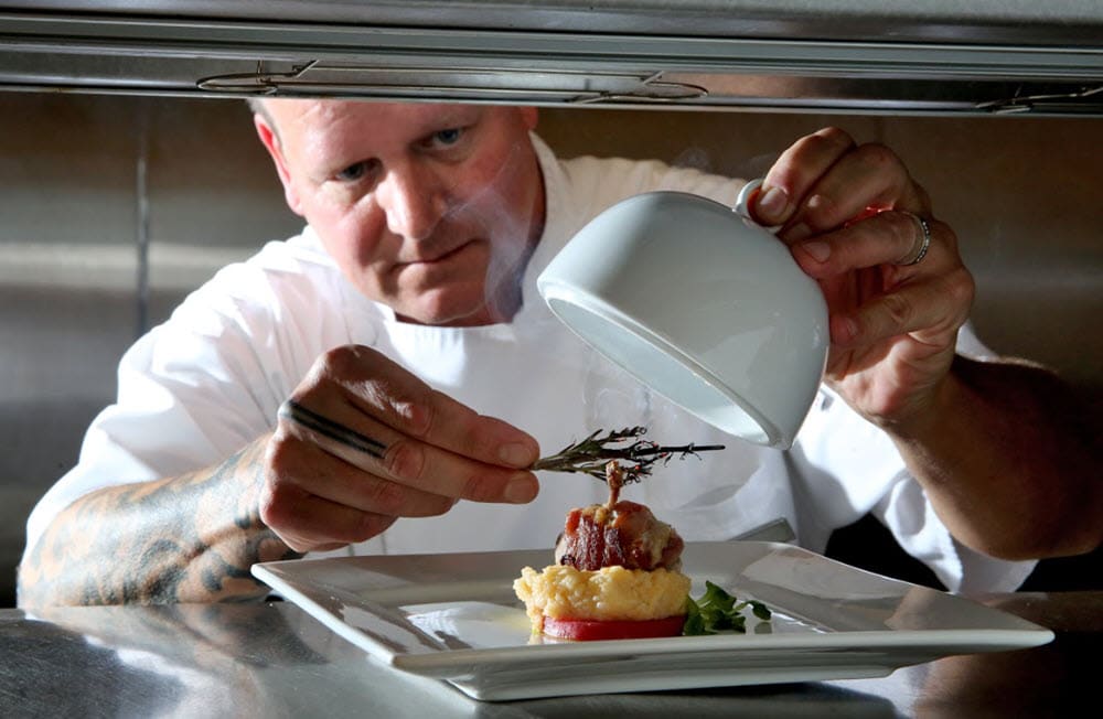 Chef delicately laying rosemary on top of a gourmet meal.